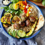 Greek meatball bowl with couscous, grilled vegetables, fresh spinach, feta, and pita bread