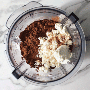 Blender filled with cocoa powder, cottage cheese, and honey before blending