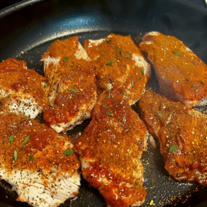 Cajun chicken breasts cooking in a skillet with spice blend