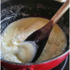 Wooden spoon stirring thickened milk mixture on stovetop