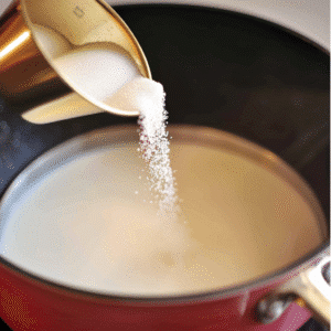 Sugar being poured into warm milk in saucepan